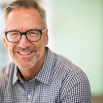 A mature, smiling man sitting outside with glasses