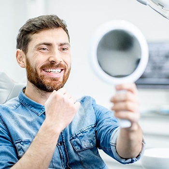 A handsome man admiring his new dental bridge in a hand mirror