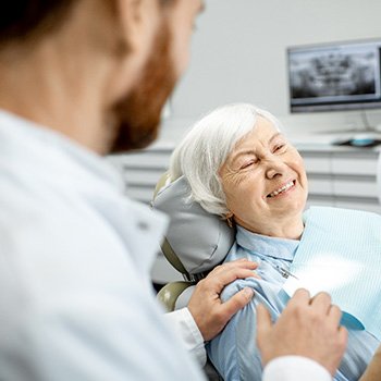 An older woman admiring her new dental implants in a hand mirror